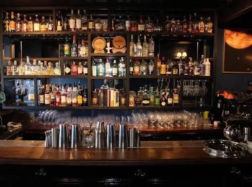 The back bar at Comptons: tiered wooden shelves stacked with whisky, gin and amaro bottles, rows of hanging glassware and a line of polished cocktail shakers along the counter.